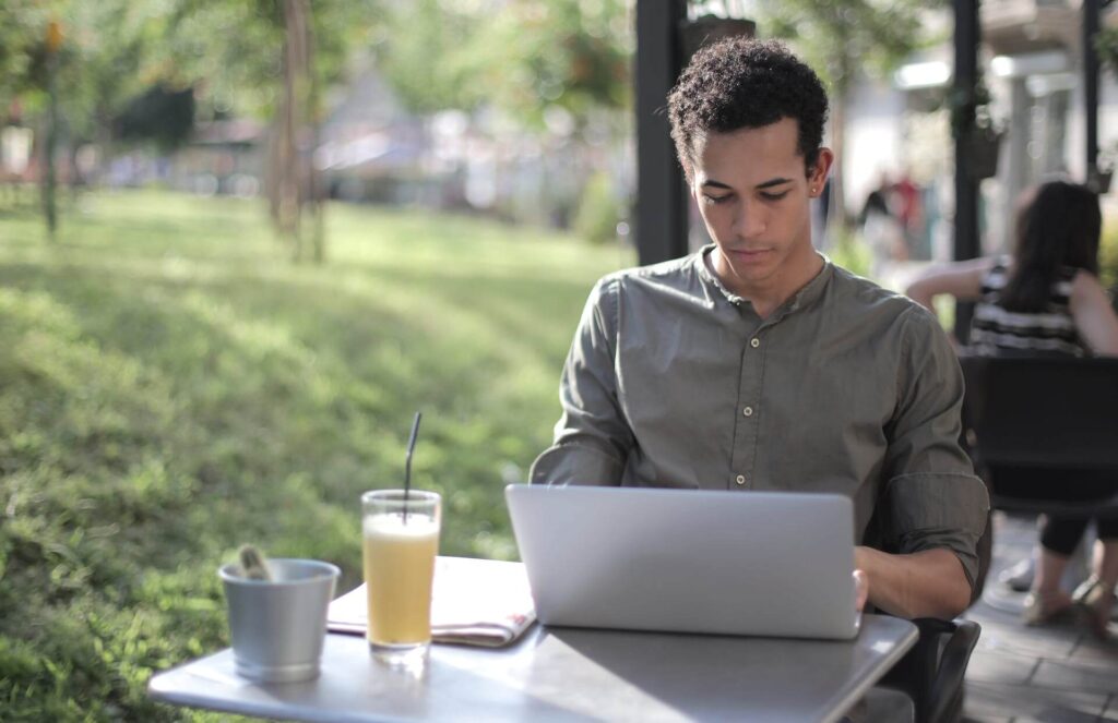 Man having a drink outside while typing on his laptop